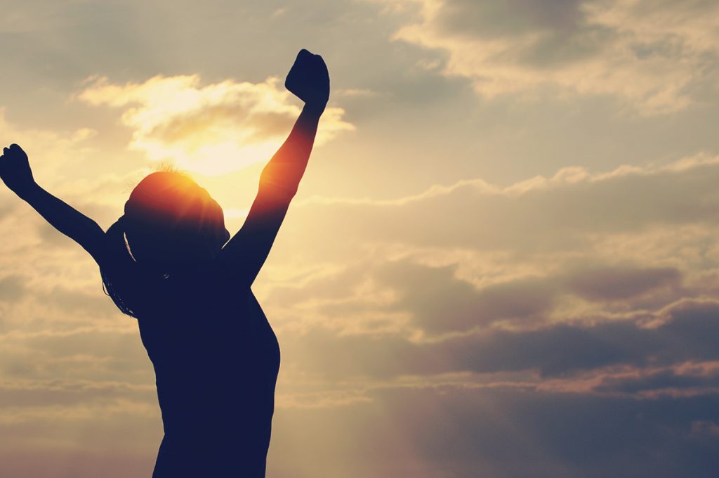 Woman happily stretching her arms during sunrise after a workout